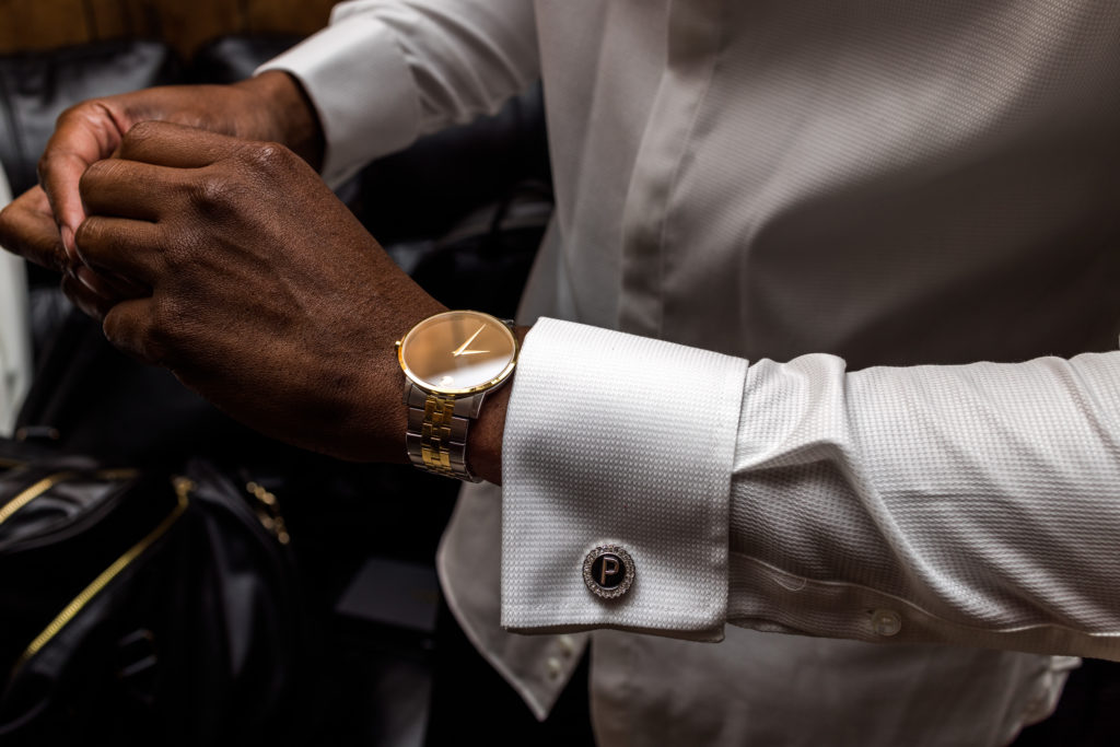 Black man with gold watch gets ready with cufflinks with the letter "P" for his last name in White Azalea Estate Groom Suite
